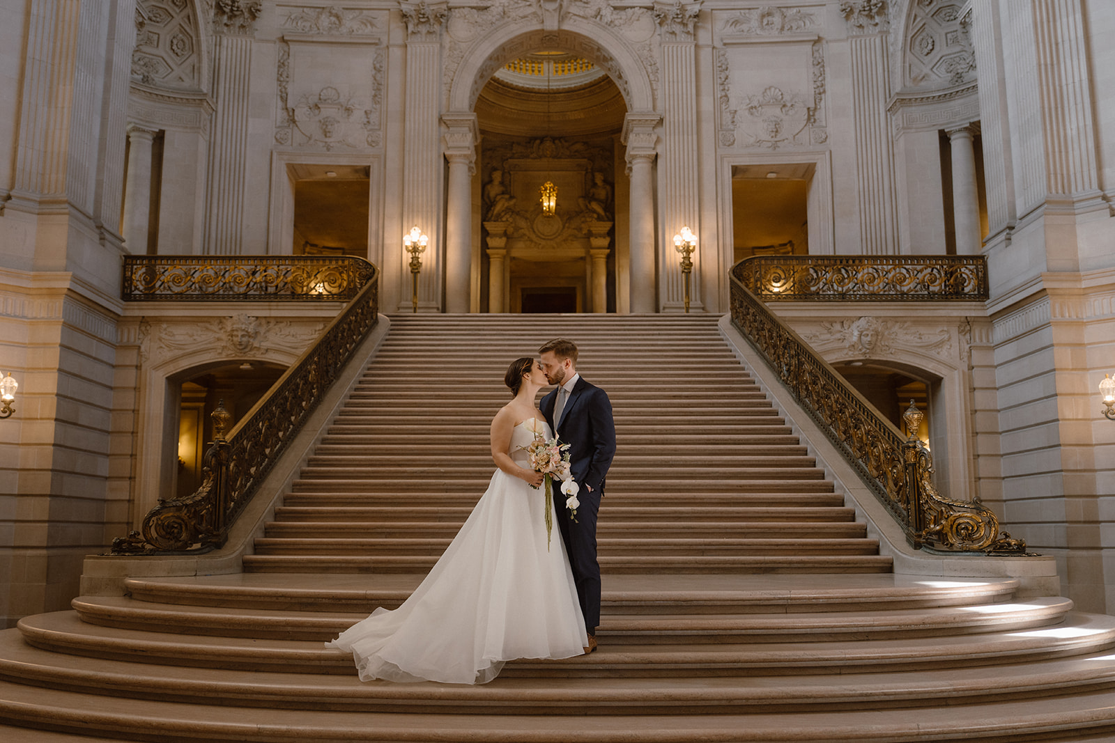 Bride and groom kiss on the grand staircase, one of the best places for San Francisco City Hall Weddings. Heech Studio & Co