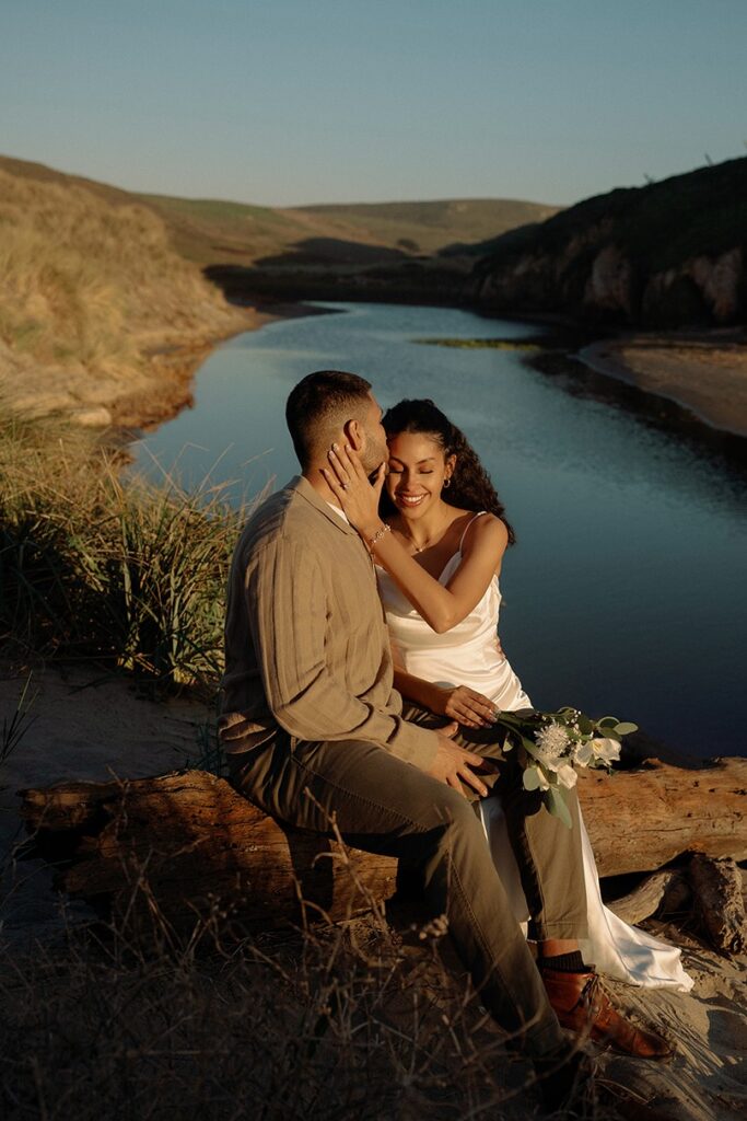 Bride and groom sitting together with the lake in the background at Point Reyes