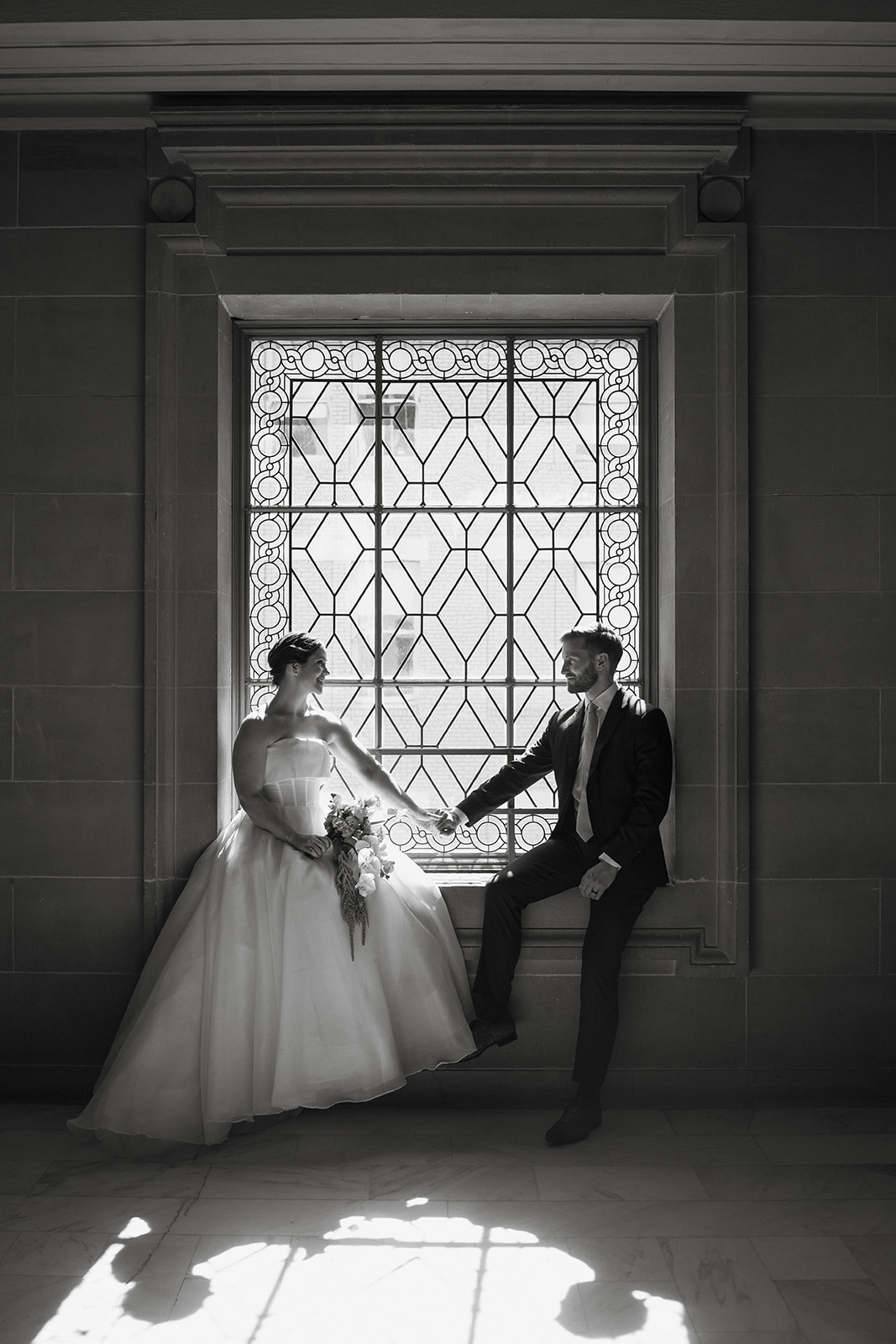 Couple sitting together in front of a window inside City Hall, captured during a San Francisco city hall wedding ceremony