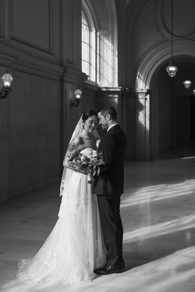 Couple standing together in soft window light inside City Hall, part of a San Francisco city hall wedding ceremony day. 