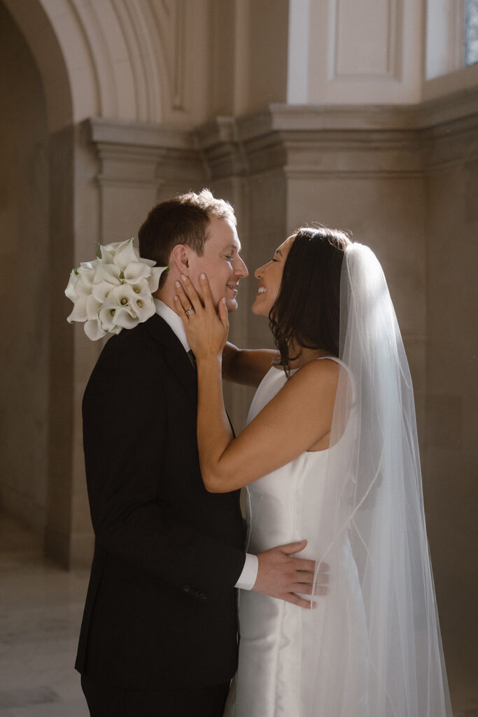 Bride holding bouquet and smiling at groom inside City Hall after their San Francisco City Hall wedding ceremony reservation. 