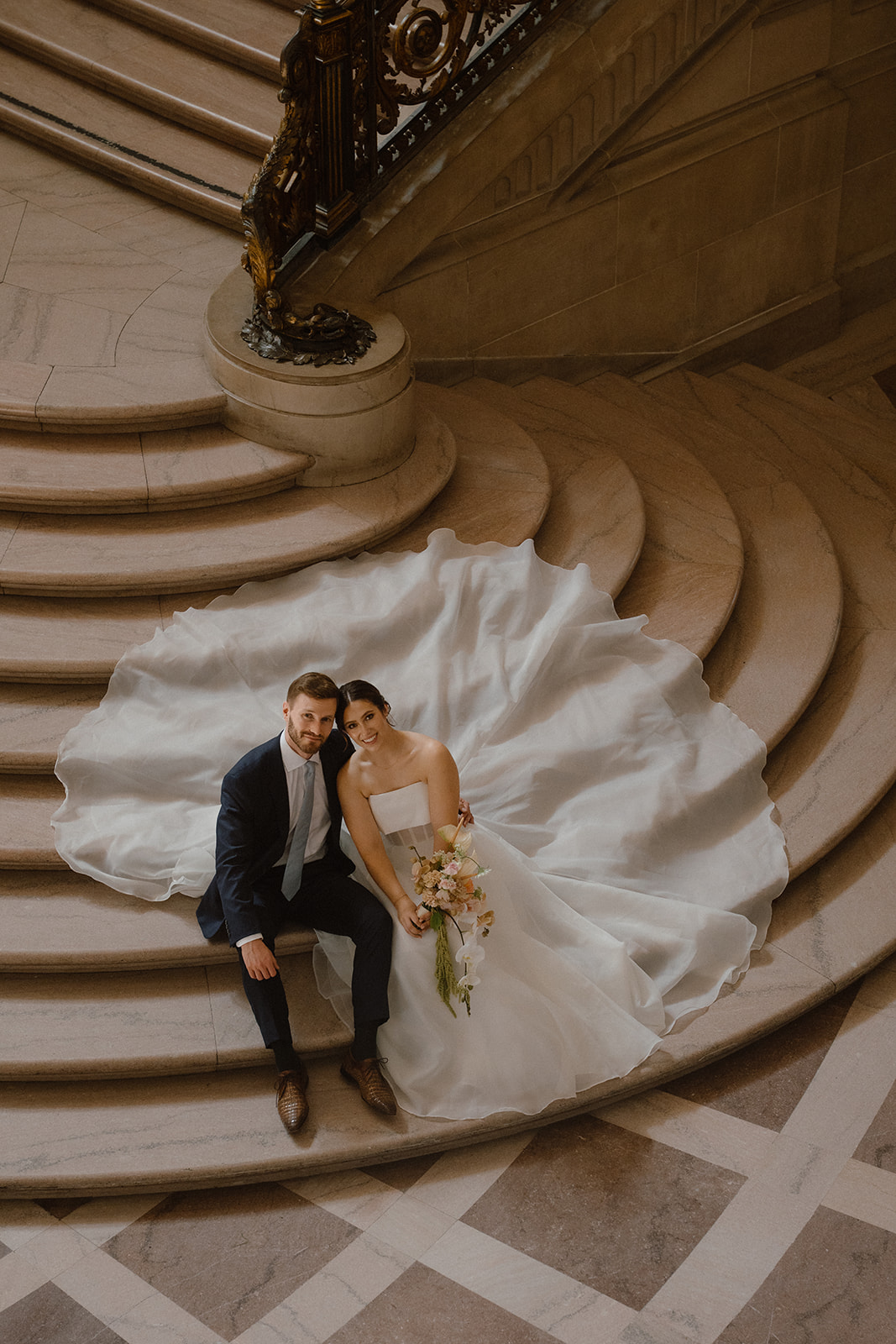 Bride and groom seated on the grand staircase inside City Hall, reflecting a San Francisco city hall wedding cost experience.