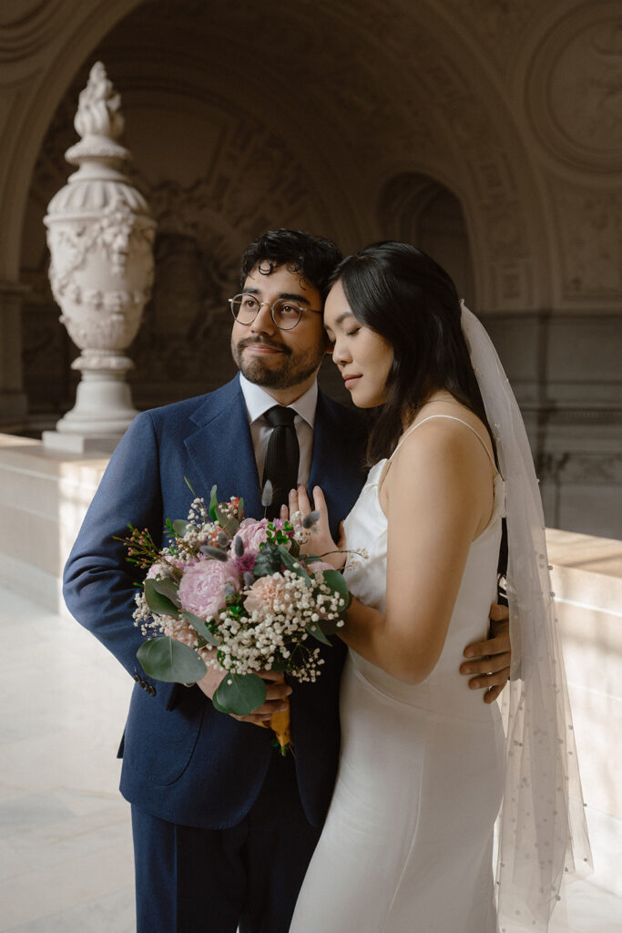 Couple holding a bouquet together inside City Hall after their SF City Hall wedding ceremony. 