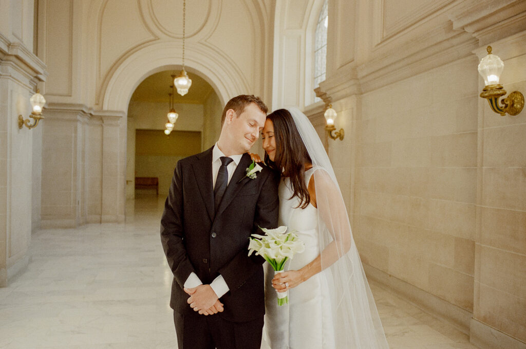 Bride leaning into groom in a softly lit hallway after their SF City Hall wedding ceremony. 