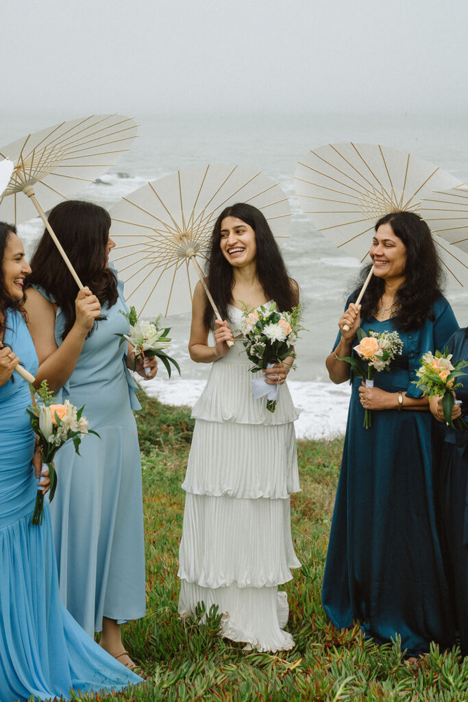 Intimate wedding with bridesmaids smiling on a cliff at Rodeo Beach in Marin Headlands