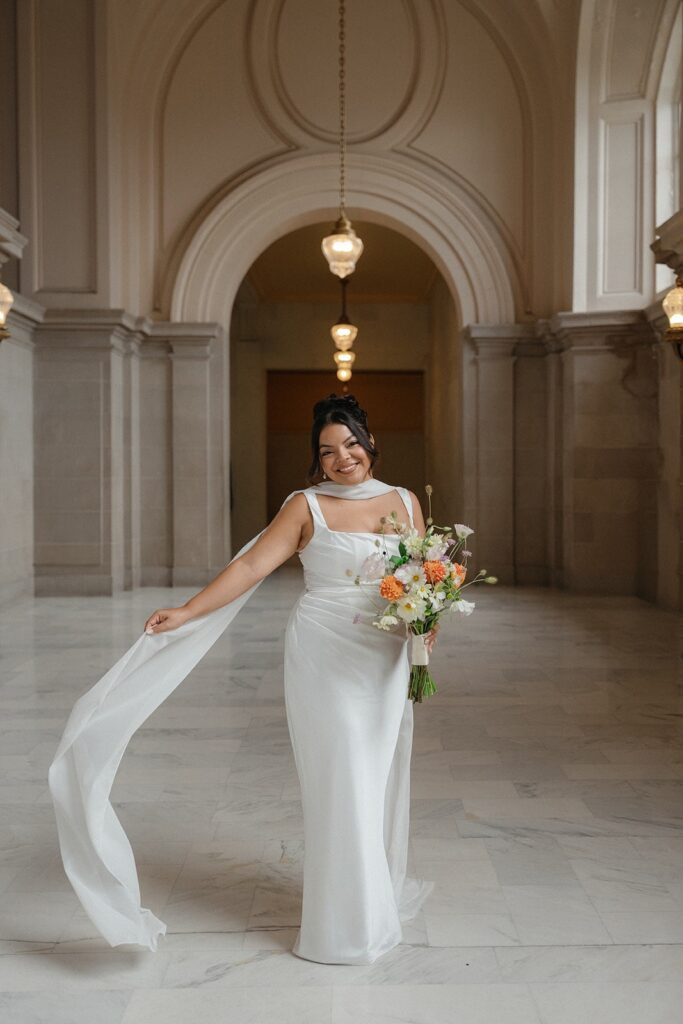 A bride waves her veil while posing for photos at her San Francisco city hall wedding