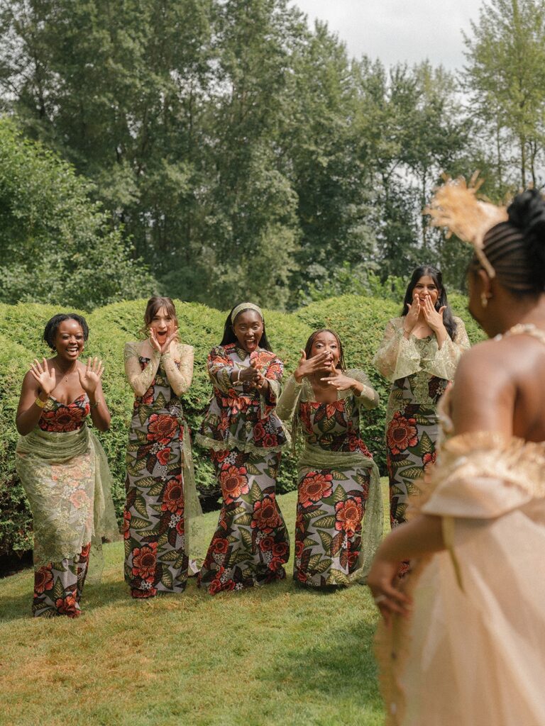A wedding party wearing green and red dresses celebrate as they see their friend in her wedding dress