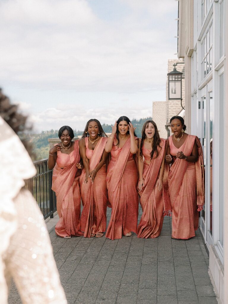 A bridal party in pink dresses cheer and smile as they see their bride friend for the first time