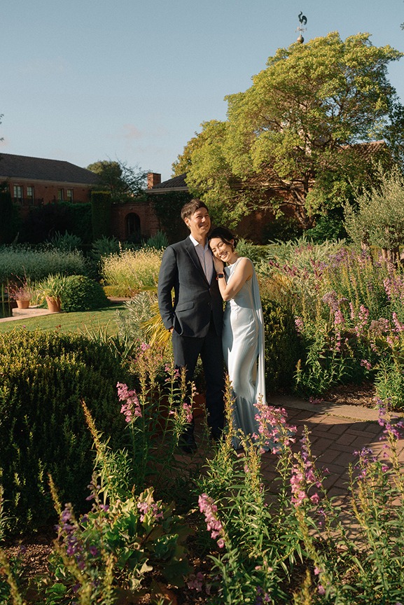 A bride and groom walk together along a path through the expansive, sun-drenched Renaissance gardens at Filoli under a clear blue sky.